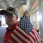 Jeff Ostrand of Bettendorf holds an American flag as he greets veterans at a previous Honor Flight of the Quad Cities’ pre-flight dinner. CREDIT DAVE THOMPSON