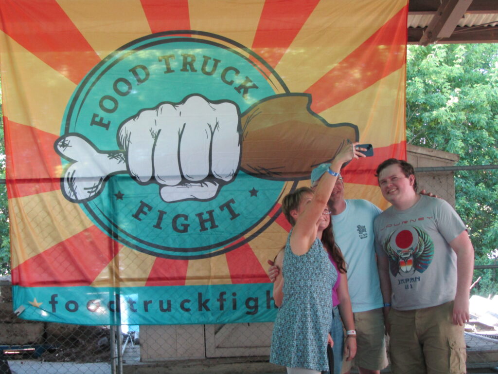 Food Truck Fight festival-goers take a selfie posing in front of a Food Truck Fight emblem on Saturday, June 18, during the event at Isle Parkway in Bettendorf.