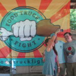 Food Truck Fight festival-goers take a selfie posing in front of a Food Truck Fight emblem on Saturday, June 18, during the event at Isle Parkway in Bettendorf.