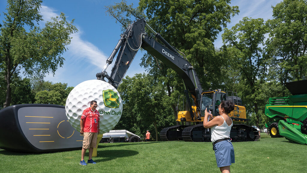 John Deere Classic fans take a minute to get a photograph Thursday, July 4, in front of the giant golf ball and driver mounted to a John Deere 470 P-tier Large Excavator at TPC Deere Run, Silvis. The driver was built by Edwards Creative Services in Milan. It weighs nearly 1,500 pounds and is big as a small bus. CREDIT TODD WELVAERT