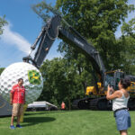 John Deere Classic fans take a minute to get a photograph Thursday, July 4, in front of the giant golf ball and driver mounted to a John Deere 470 P-tier Large Excavator at TPC Deere Run, Silvis. The driver was built by Edwards Creative Services in Milan. It weighs nearly 1,500 pounds and is big as a small bus. CREDIT TODD WELVAERT