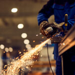 Worker performing grinding task in an industrial setting with bright flying sparks.