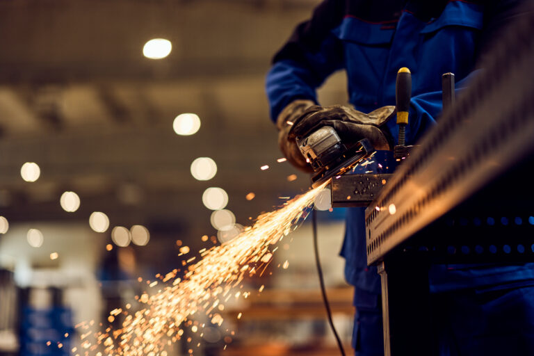Worker performing grinding task in an industrial setting with bright flying sparks.