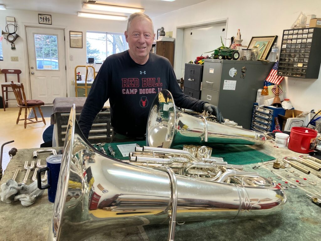 Lee Stofer with two of his restored tubas in his instrument shop in Camanche. CREDIT JONATHAN TURNER